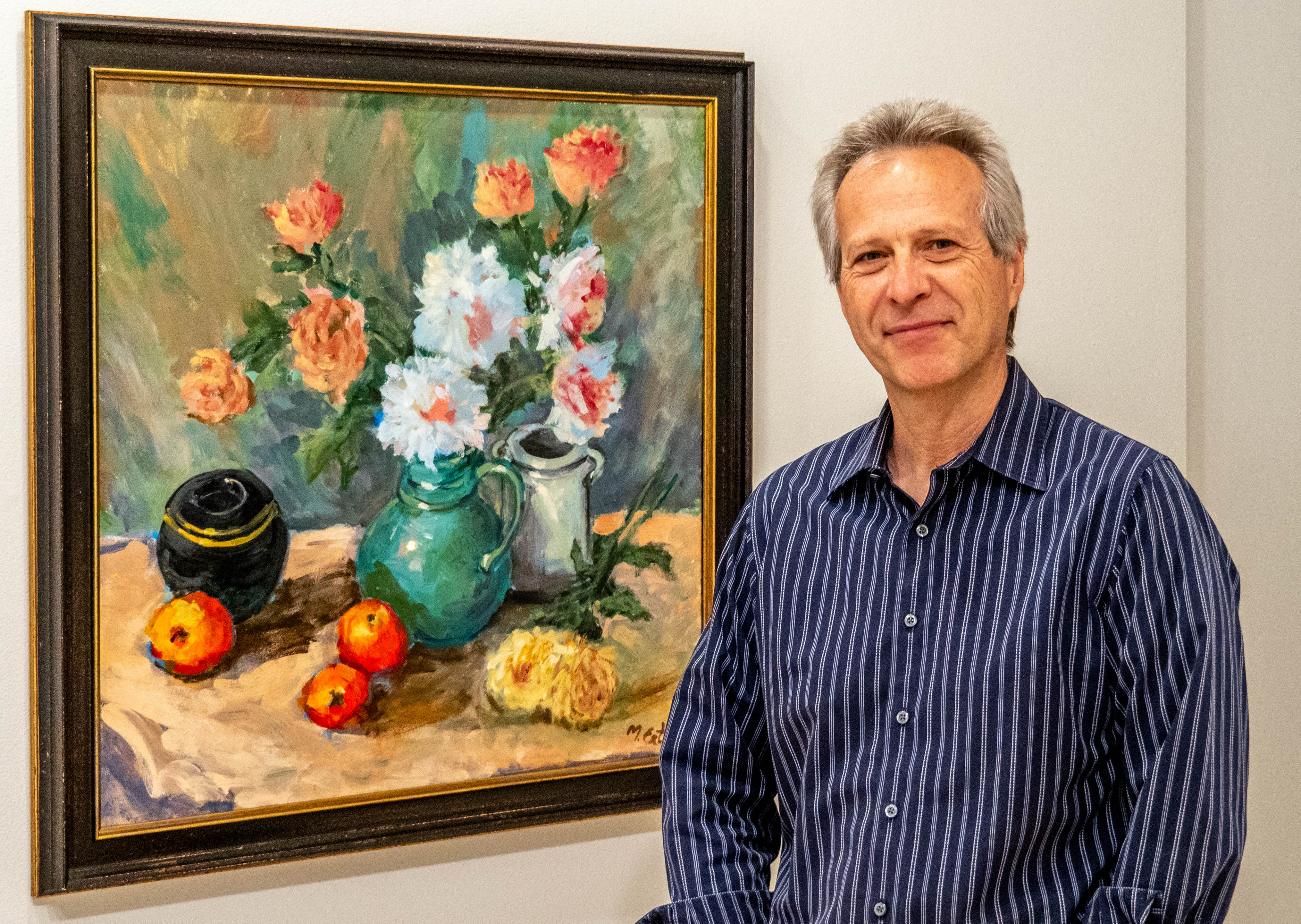 Mutlu Ertaç standing beside a still life of flowers and fruit